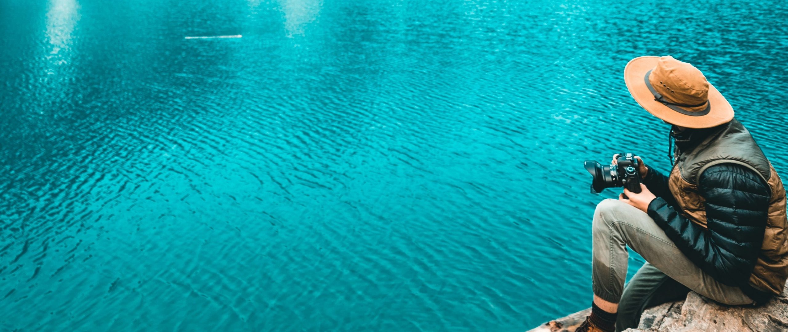 Photographer sitting near a body of ice blue water with a camera