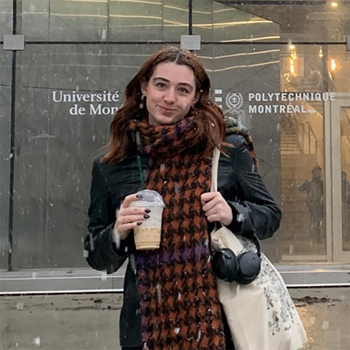 Eden Grimes standing outside in Montreal holding an iced coffee, headphones and a bag