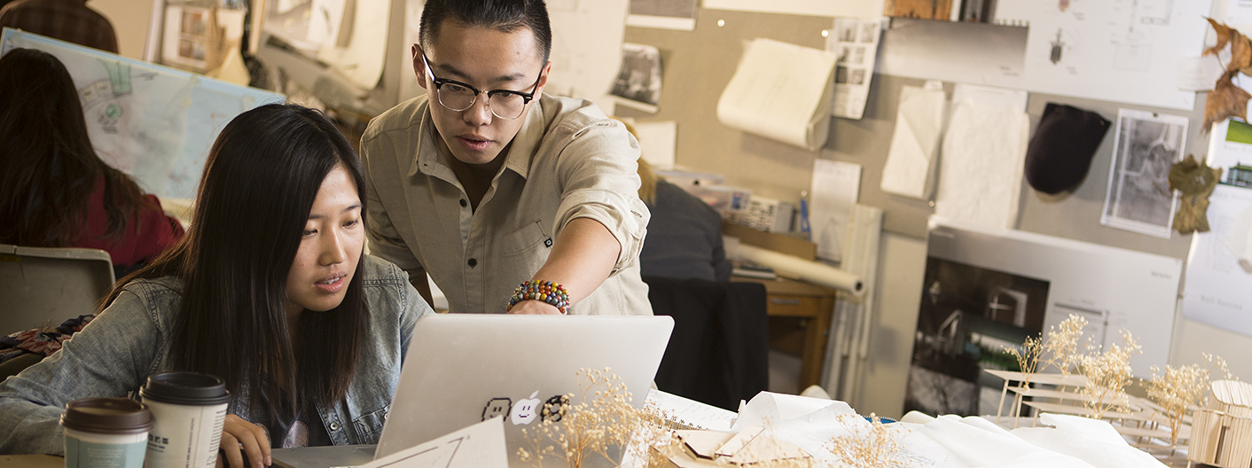 Design students looking over a project on a laptop surrounded by other projects