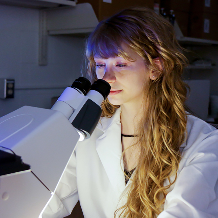 A female student looking at an item under a microscope