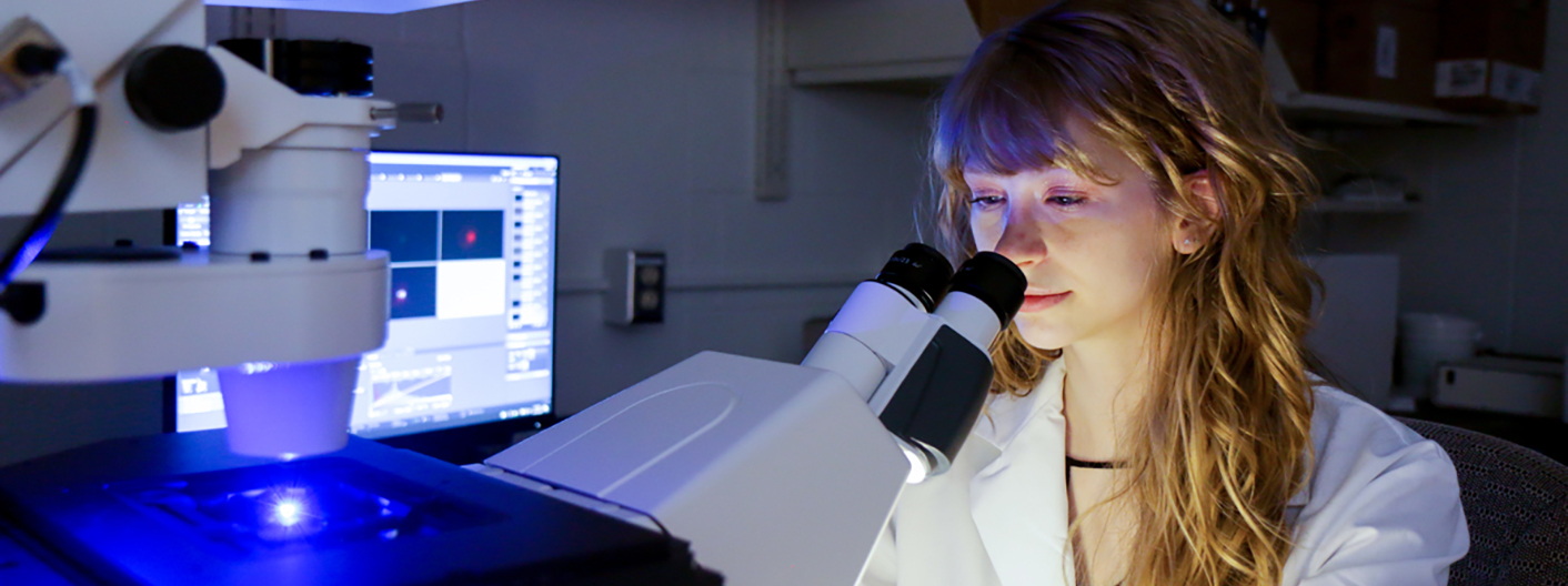 A female student looks at an item under the microscope