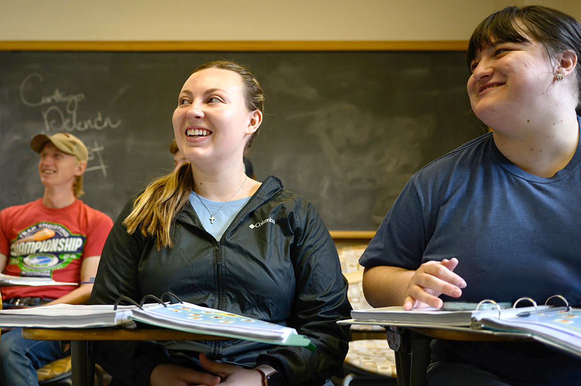 Three students smiling while listening to a lecture in class
